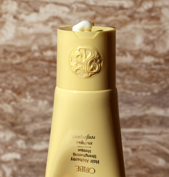 A small dollop of Oribe Hair Alchemy Strengthening Masque is squeezed from bottle against a brown marbled background
