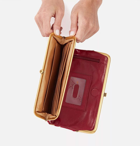 Model's hands hold open a red leather wallet frame compartment to reveal gold lining with card slots