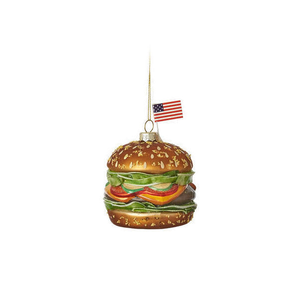 Painted glass ornament resembles a hamburger with an American flag stuck in the bun