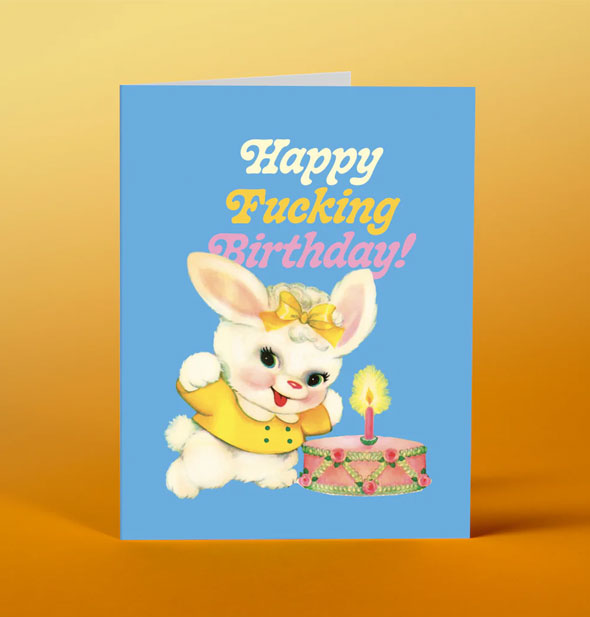 Blue greeting card with illustration of a smiling white bunny wearing yellow shirt and bow with cake says, "Happy Fucking Birthday!"
