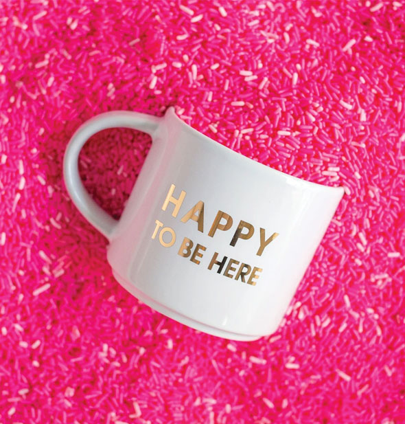 Happy to Be Here mug is partially buried in a pile of pink sprinkles