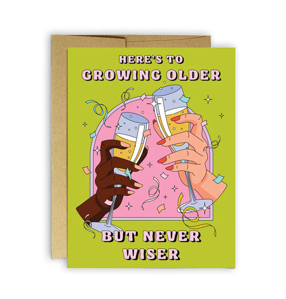 Green birthday card with kraft envelope behind features illustration of two hands holding champagne glasses amid confetti with the words, "Here's to growing older but never wiser" in pink lettering