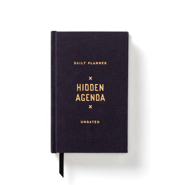 Cloth bound book with ribbon bookmark extending from the bottom says, "Daily Planner x Hidden Agenda x Undated" in metallic gold foil