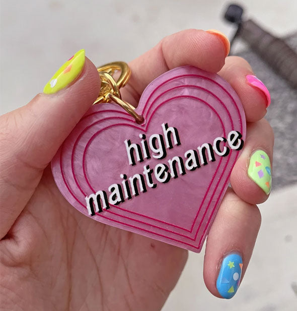 Model's hand holds a pink heart-shaped High Maintenance keychain
