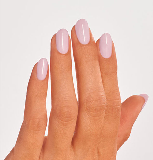 Model's hand wears a light pastel shade of pink nail polish