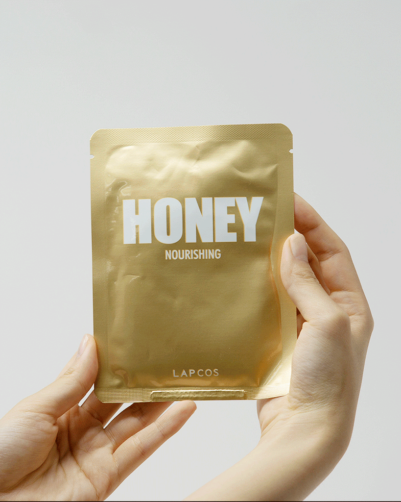 Model's hands remove and unfold a sheet mask from a gold Honey Nourishing packet