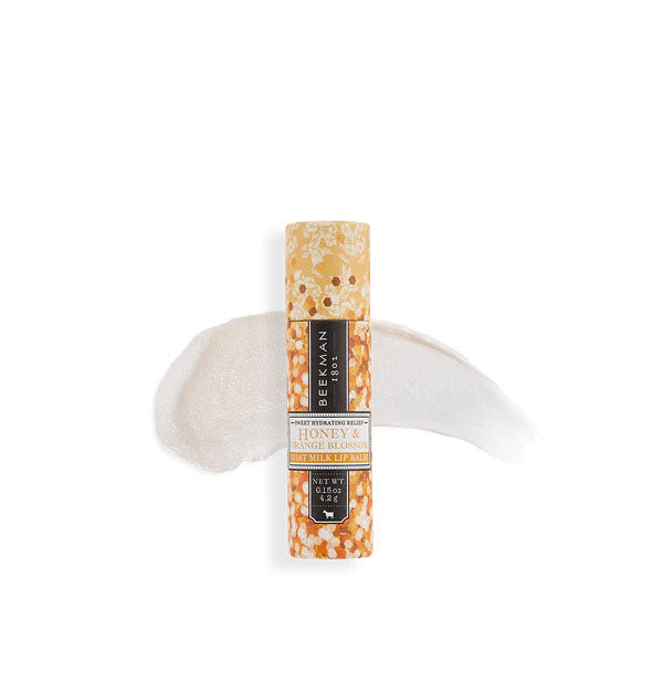 Decorative orange floral tube of Beekman 1802 Honey & Orange Blossom lip balm with sample product application behind