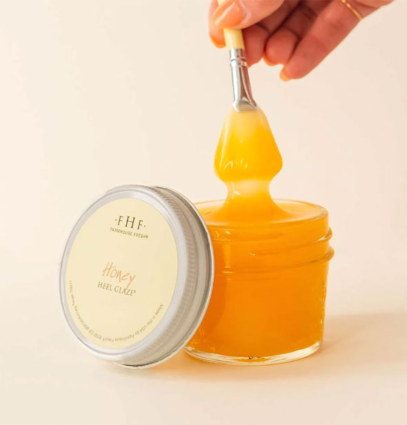 Model's hand pulls a saturated brush from a pot of Honey Heel Glaze; lid sits upright to the side