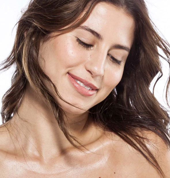 Smiling model glistens with an application of body oil on décolletage 