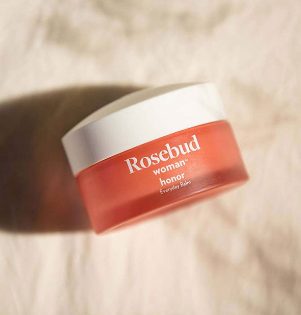 Coral-colored jar of Rosebud Woman Honor Everyday Balm with white lid on a marbled surface