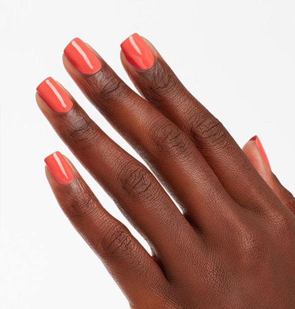 Model's hand wears a pinkish-orange shade of nail polish