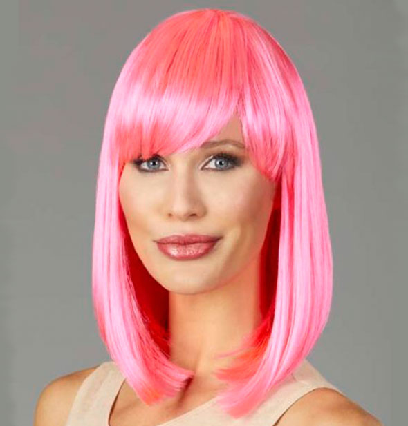 Model wearing a shoulder length, pink wig with bangs.