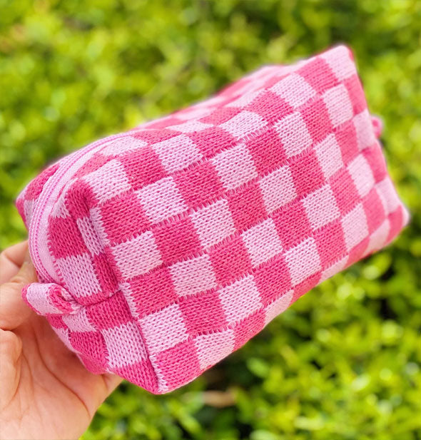 Model's hand holds a light pink and dark pink checker print knit makeup bag