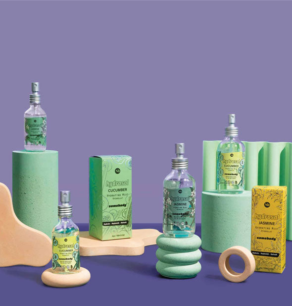2- and 4-ounce bottles of Somebody brand Cucumber and Jasmine hydrosol sprays staged with peach and aqua geometric structural shapes against a purple background
