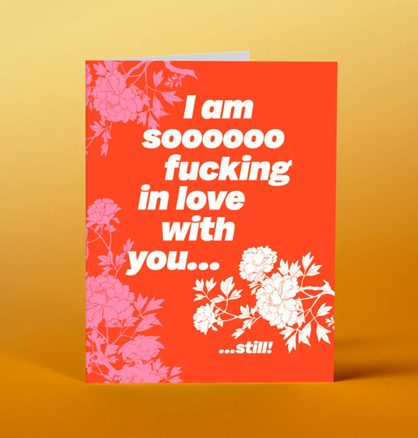 Red greeting card with pink and white floral designs says, "I amm soooooo fucking in love with you...still!"