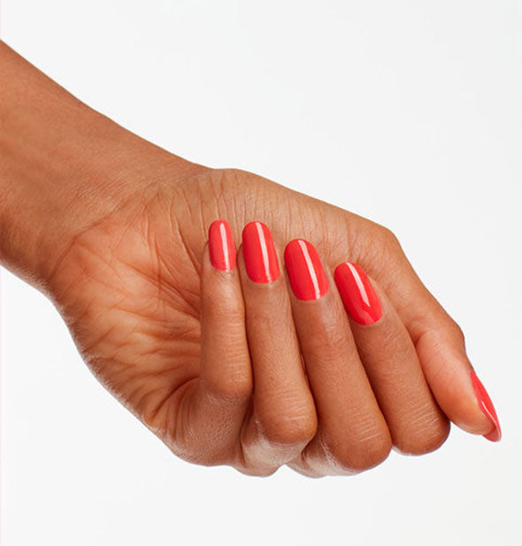 Model's hand wears a bright orangey-pink shade of nail polish
