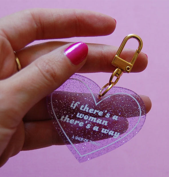 Model's hand holds heart-shaped If There's a Woman There's a Way keychain for size reference