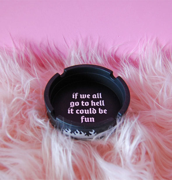 Round black silicone ashtray with flames design on the side says, "If we all go to hell it could be fun" in pink lettering on its interior