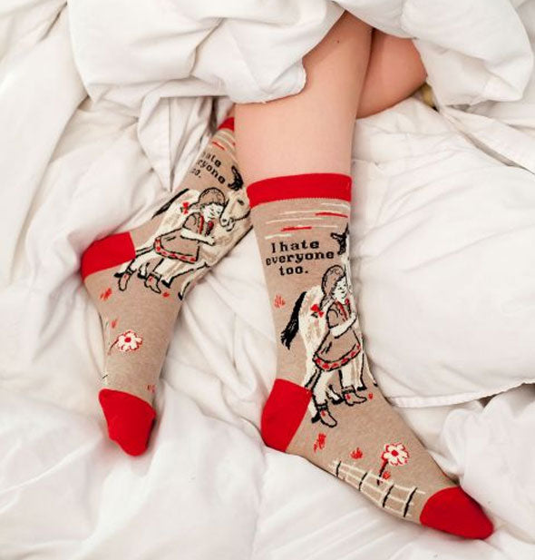 A model whose legs are sticking out from white bedding wears a pair of I Hate Everyone Too socks