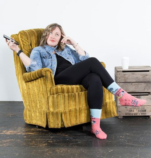 Model sitting in a chartreuse velvet armchair wears a pair of I Heard You and I Don't Care socks