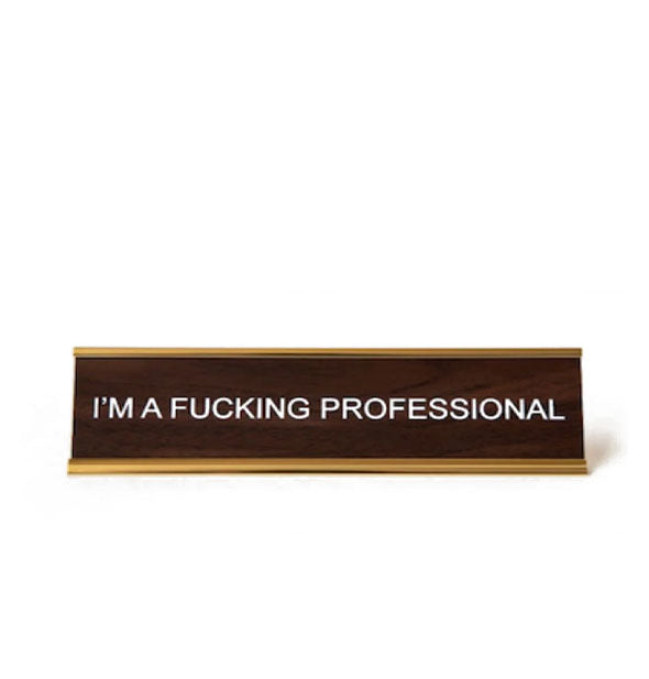 Rectangular faux wood and gold desk sign says, "I'm a fucking professional" in white lettering