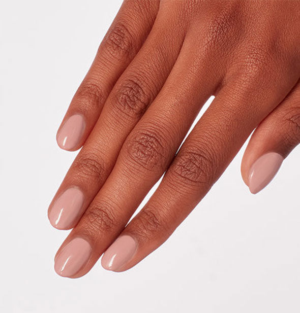 Model's hand wears a neutral pink shade of nail polish