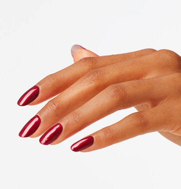 Model's hand wears a dark shimmery red shade of nail polish