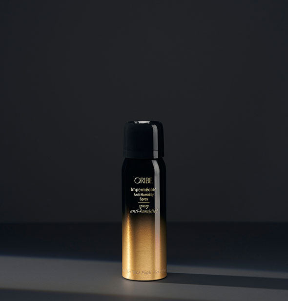 Small black and gold can of Oribe Imperméable Anti-Humidity Spray on a dark gray background
