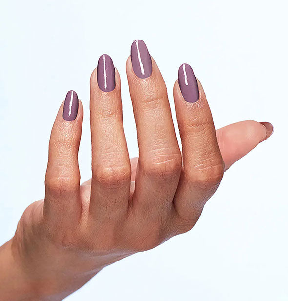 Model wears a muted shade of medium-dark purple-mauve nail polish