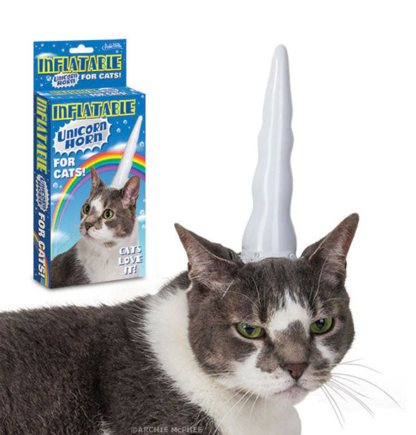 An angry-looking grey and white cat wears a white unicorn horn on top of its head underneath product packaging