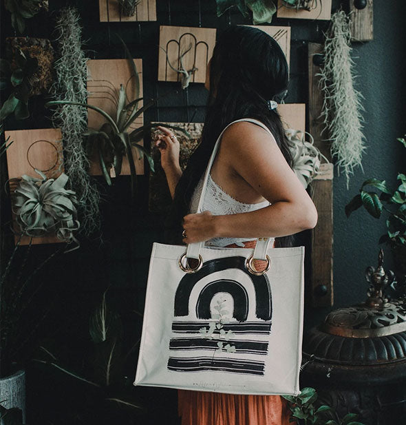 Model poses with a white tote bag with black brushstroke design over her shoulder