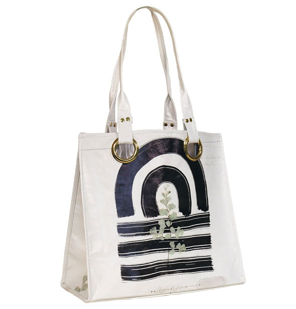White tote bag with bold, black brushstroke design, hand-pressed leaf accent, and gold handle hardware