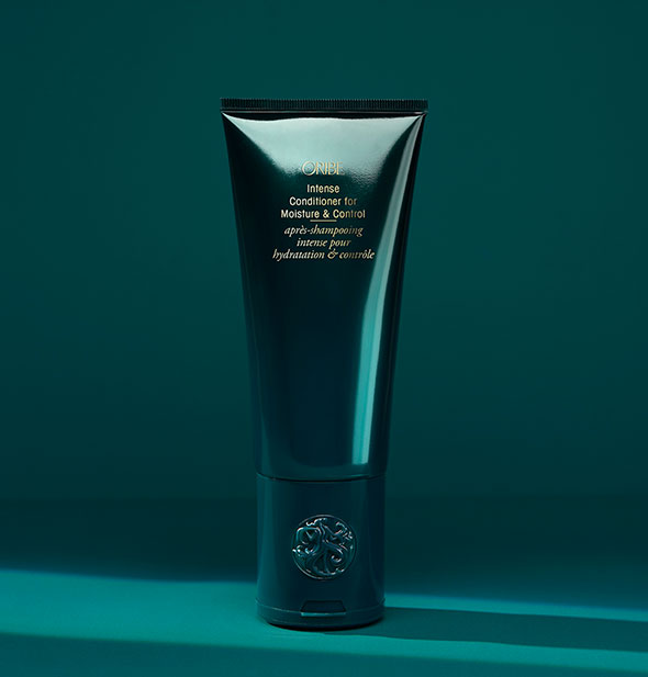 Dark teal bottle of Oribe Intense Conditioner for Moisture & Control on teal background