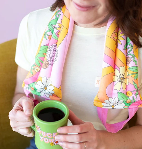 Model holding green coffee cup wears a colorful retro-style floral print neck wrap with pink handles