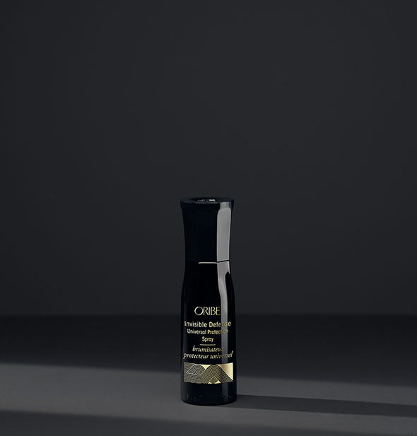 Small black bottle of Oribe Invisible Defense Universal Protection Spray on dark gray background