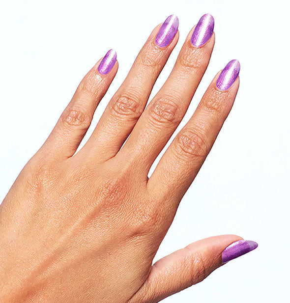 Model's hand wears a shimmery shade of purple nail polish on clear acrylics