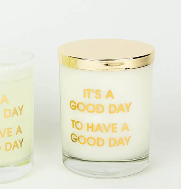 A glass candle with gold lid and the phrase "It's a Good Day to Have a Good Day" printed in gold foil.
