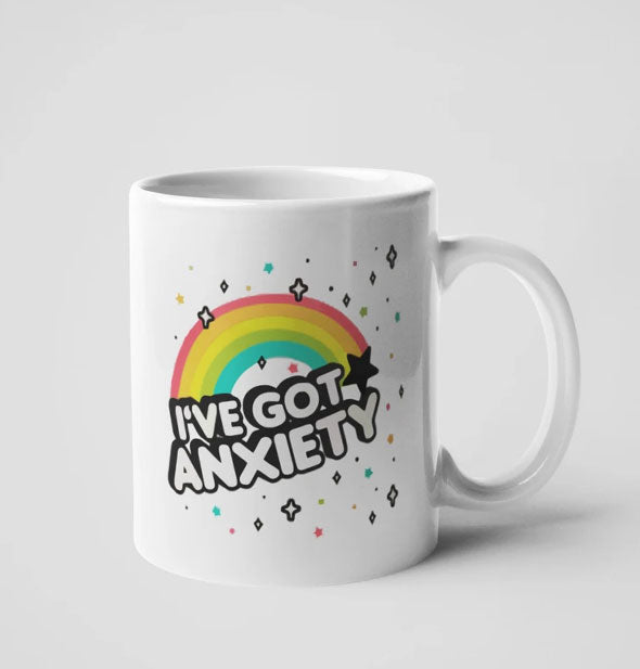 White coffee mug with rainbow and stars design says, "I've Got Anxiety"