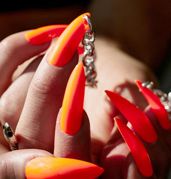 Model's hands wearing long orange nails joined in some places by thick silver chain