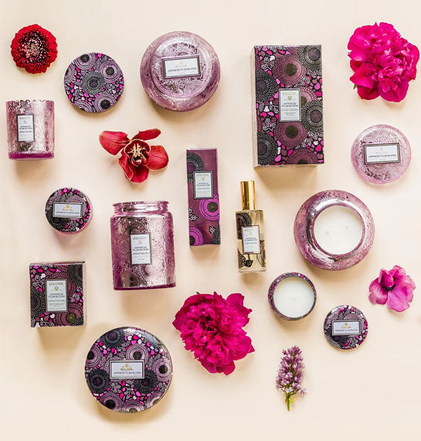 An assortment of Japanese Plum Bloom Voluspa products staged with red and pink flowers