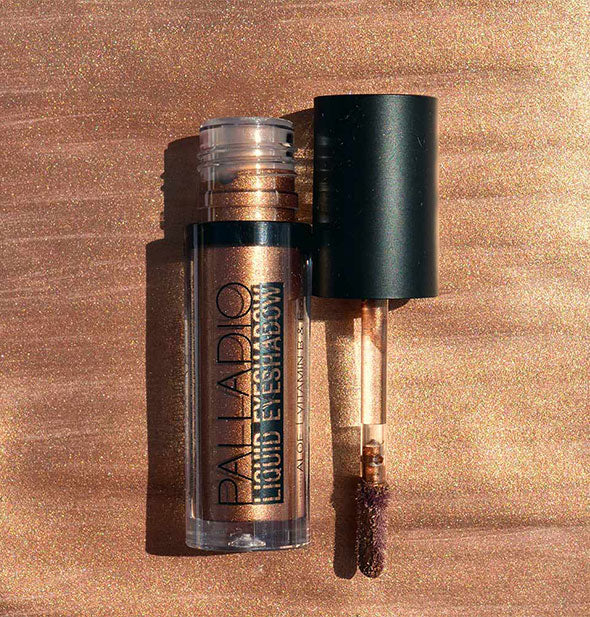 Tube of Palladio Liquid Eyeshadow with applicator wand removed against background sample color swatch in a rich metallic copper shade
