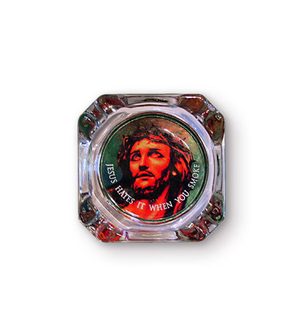 Square glass ashtray with beveled corners features central design of Jesus wearing a crown of thorns with the words, "Jesus hates it when you smoke" in white lettering