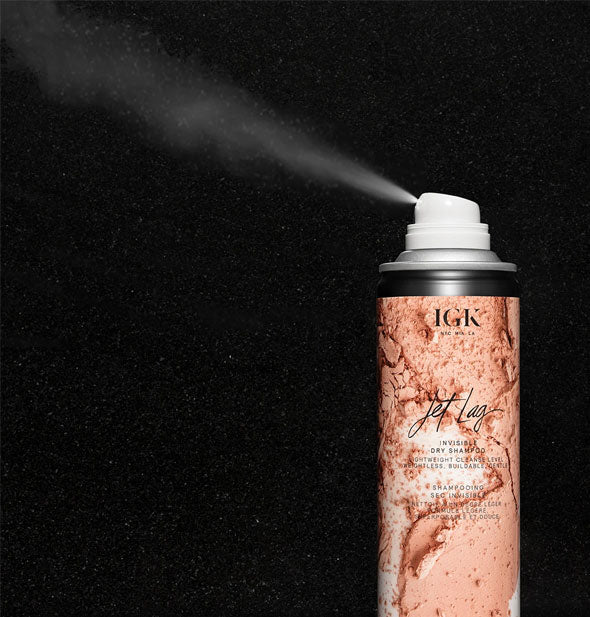 An application of IGK Jet Lag Invisible Dry Shampoo is dispensed from can against a black background