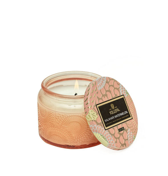 Peach-colored embossed glass jar candle with decorative metallic lid set to the side