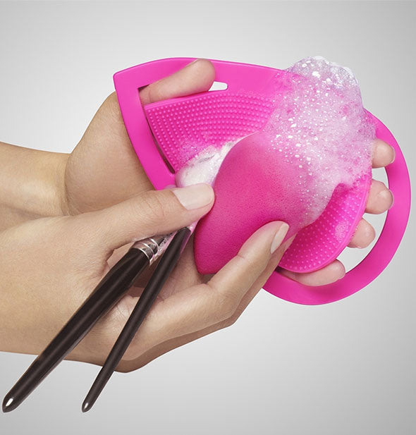 Model demonstrates how to use a handheld makeup brush and sponge cleaning pad