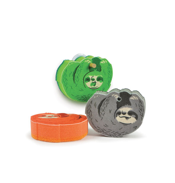 Set of three sloth sponges in green, gray, and orange, each with a hole for hanging on a wooden peg