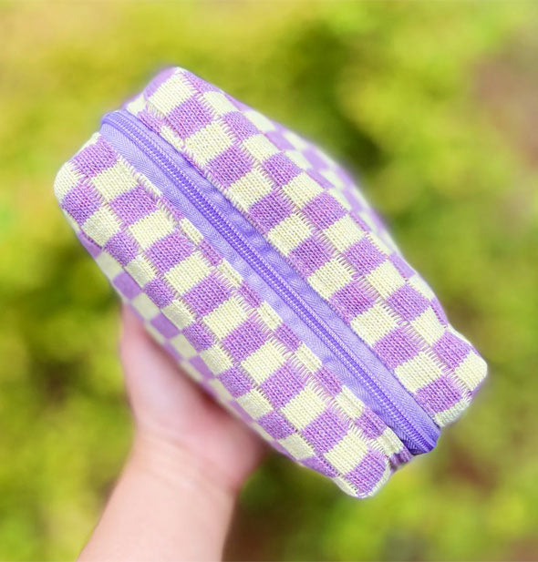 Model's hand holds a purple and white checker print knit makeup bag