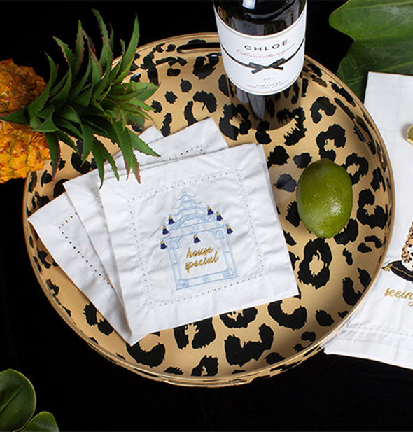 Round leopard print serving tray holds cocktail napkins, a bottle of wine, and a lime