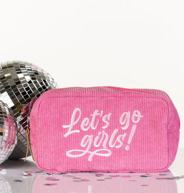 Pink corduroy Let's Go Girls! cosmetic pouch is staged with mini disco balls and confetti on a reflective surface