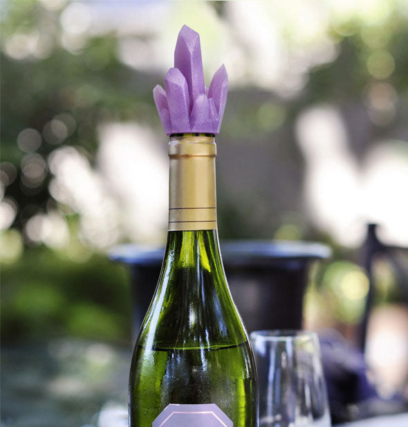 Purple crystal cluster bottle stopper shown corking a wine bottle against an outdoor backdrop